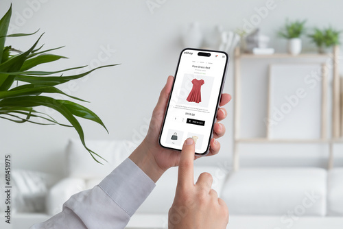 Woman shopping online with smart phone. Buying a red flow dress on ecommerce web page. Living room interior in background