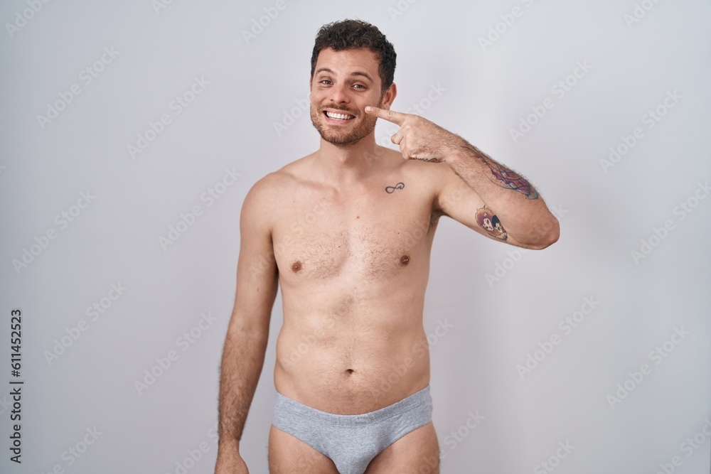 Young hispanic man standing shirtless wearing underware pointing with hand finger to face and nose, smiling cheerful. beauty concept