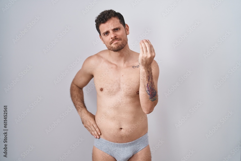 Young hispanic man standing shirtless wearing underware doing italian gesture with hand and fingers confident expression