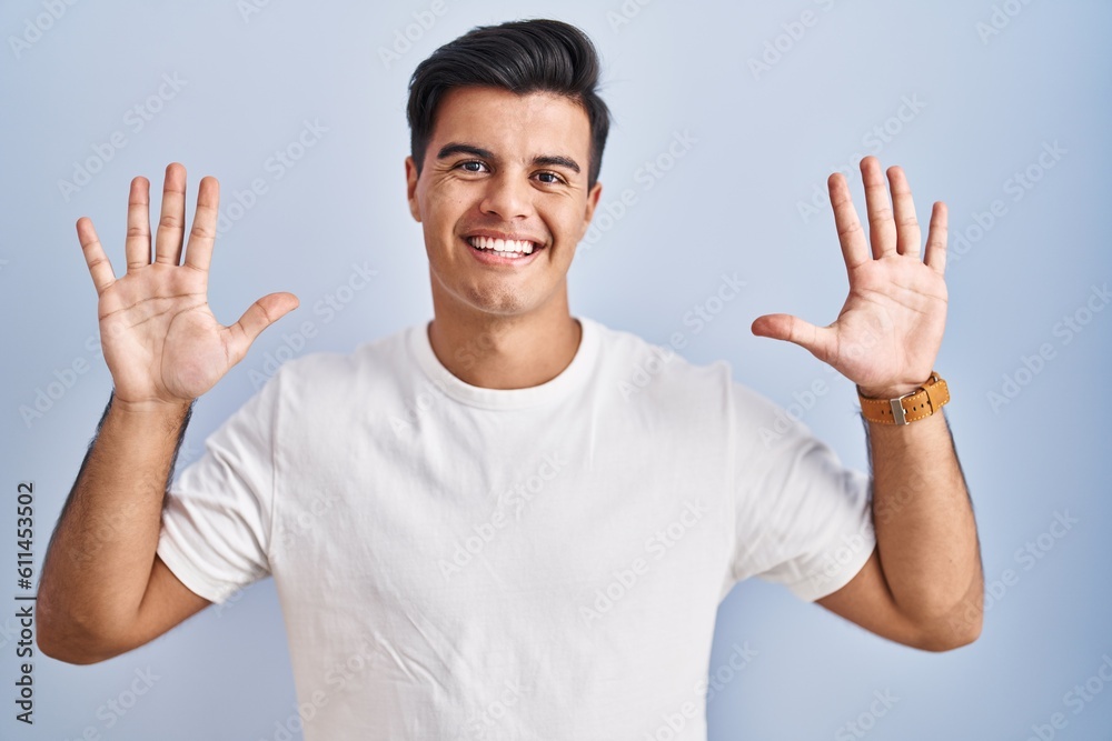 Hispanic man standing over blue background showing and pointing up with fingers number ten while smiling confident and happy. Hispanic man standing over blue background showing and pointing up with fingers number ten while smiling confident and happy.