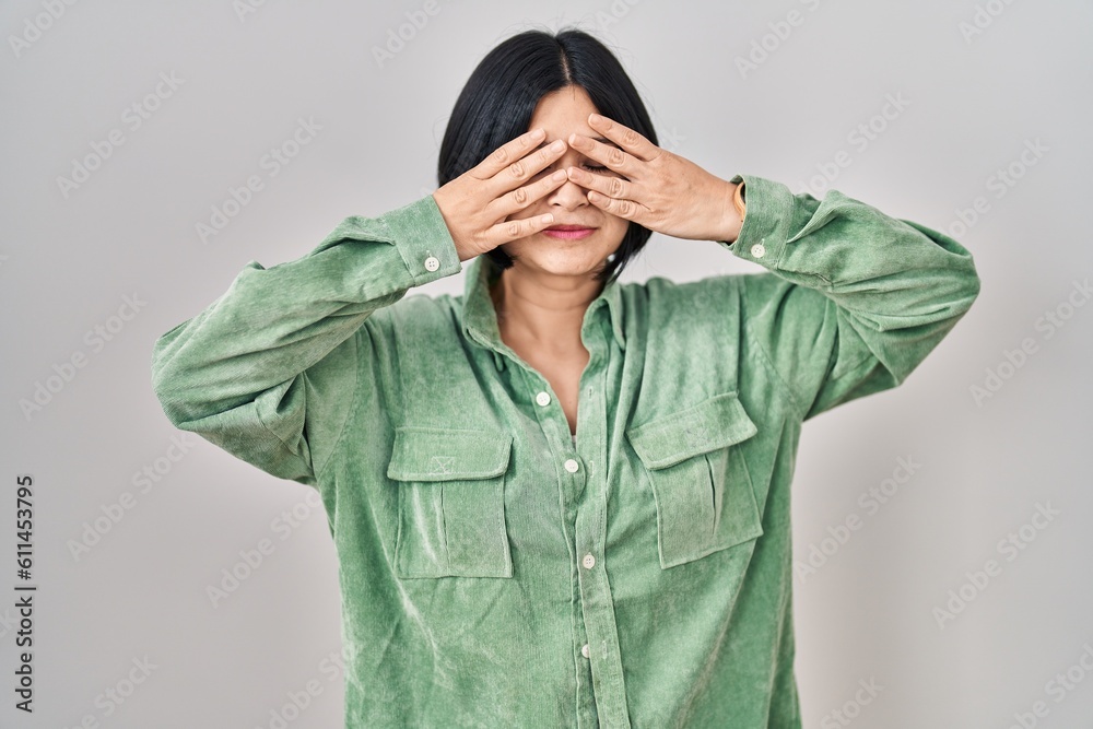 Young asian woman standing over white background covering eyes with hands smiling cheerful and funny. blind concept. Young asian woman standing over white background covering eyes with hands smiling cheerful and funny. blind concept.