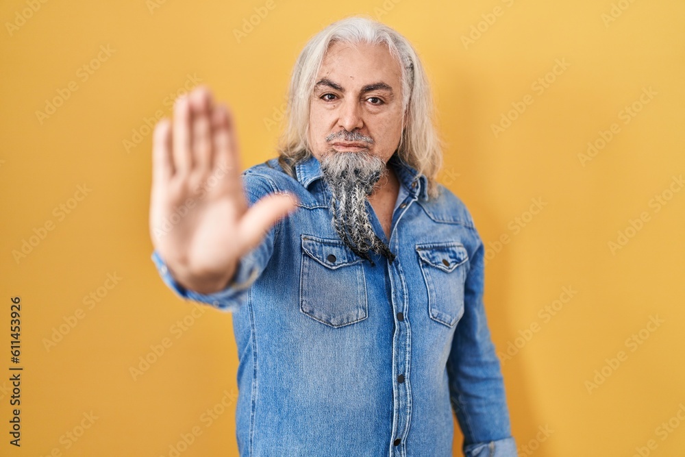 Middle age man with grey hair standing over yellow background doing stop sing with palm of the hand. warning expression with negative and serious gesture on the face. Middle age man with grey hair standing over yellow background doing stop sing with palm of the hand. warning expression with negative and serious gesture on the face.