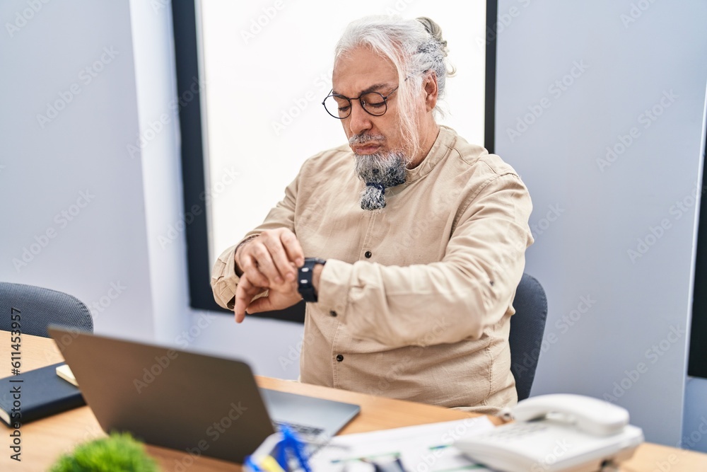 Middle age grey-haired man business worker using laptop looking watch at office Middle age grey-haired man business worker using laptop looking watch at office