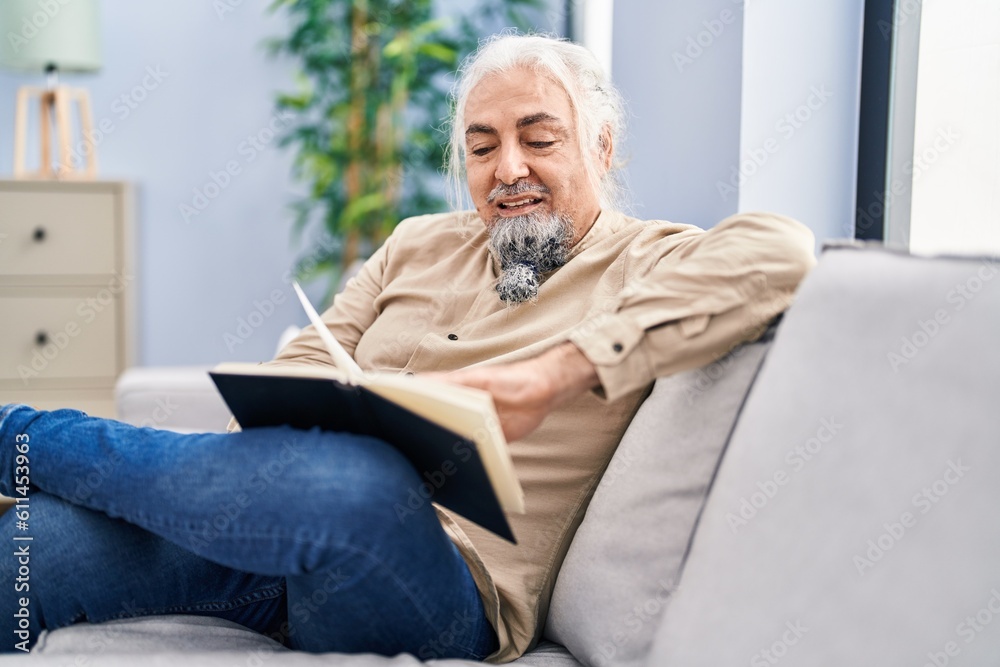 Middle age grey-haired man reading book sitting on sofa at home Middle age grey-haired man reading book sitting on sofa at home