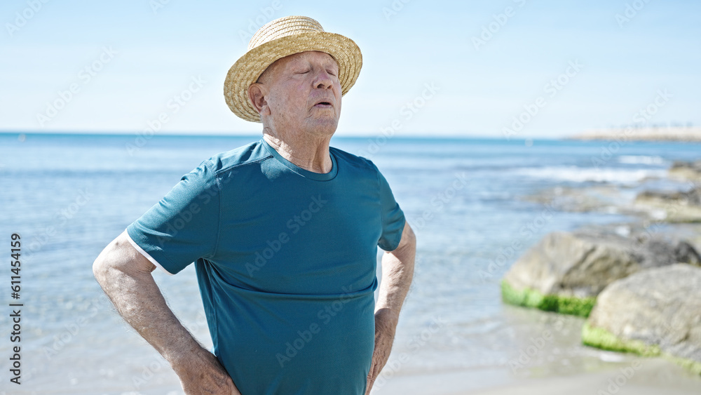 Senior grey-haired man tourist wearing summer hat breathing at seaside