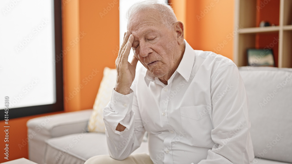 Fototapeta premium Senior grey-haired man worried with hand on forehead at home