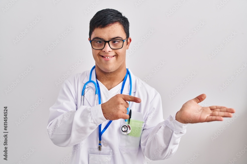 Young hispanic man with down syndrome wearing doctor uniform and stethoscope amazed and smiling to the camera while presenting with hand and pointing with finger. Young hispanic man with down syndrome wearing doctor uniform and stethoscope amazed and smiling to the camera while presenting with hand and pointing with finger.