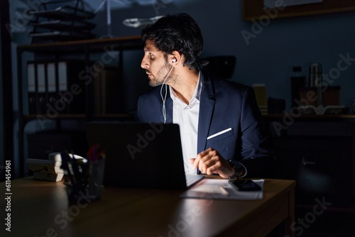 Handsome latin man working at the office at night looking to side, relax profile pose with natural face with confident smile.