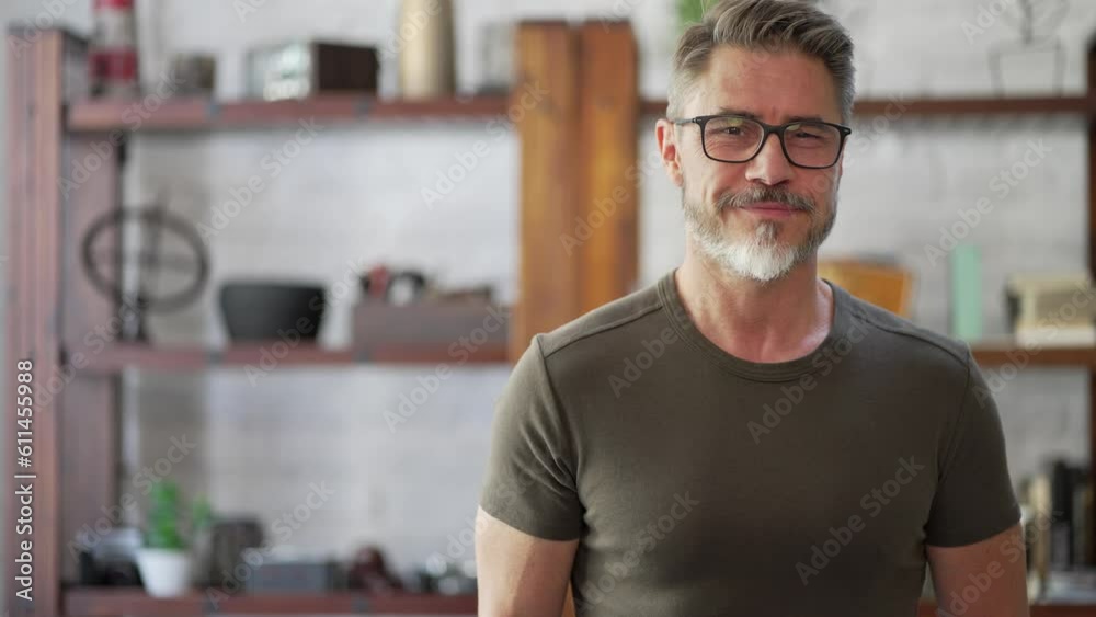 Portrait of happy, confident older man at home looking at camera smiling. Mature age, middle age, mid adult casual guy in 50s, bearded, gray hair, wearing glasses.