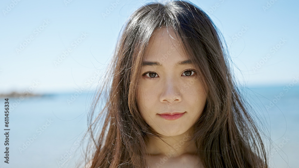 Young chinese woman standing with serious expression at seaside