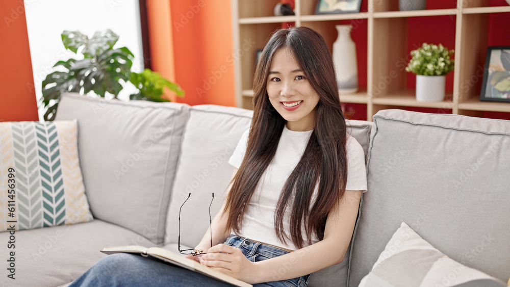 Young chinese woman reading book sitting on sofa at home Young chinese woman reading book sitting on sofa at home