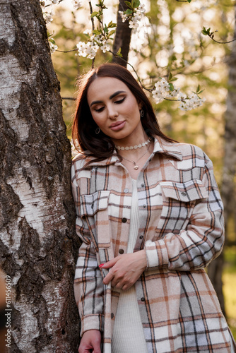 A girl in a plaid is standing near a flowering tree. Portrait of a beautiful young woman