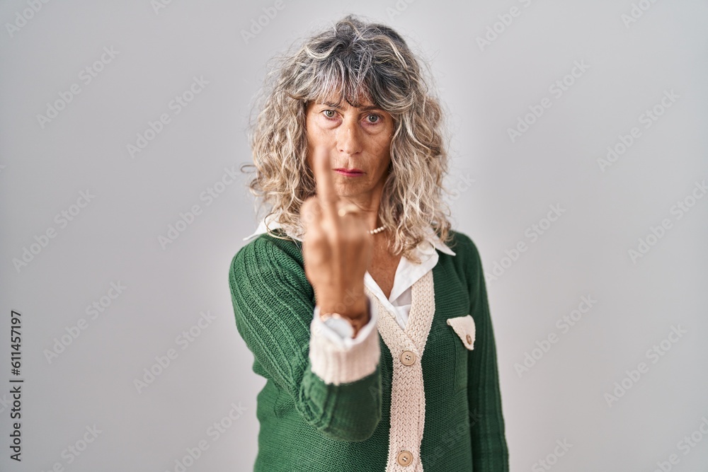 Middle age woman standing over white background showing middle finger, impolite and rude fuck off expression Middle age woman standing over white background showing middle finger, impolite and rude fuck off expression