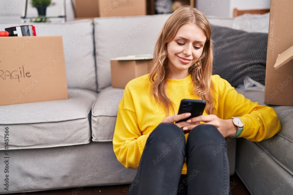 Young blonde woman using smartphone sitting on floor at new home Young blonde woman using smartphone sitting on floor at new home