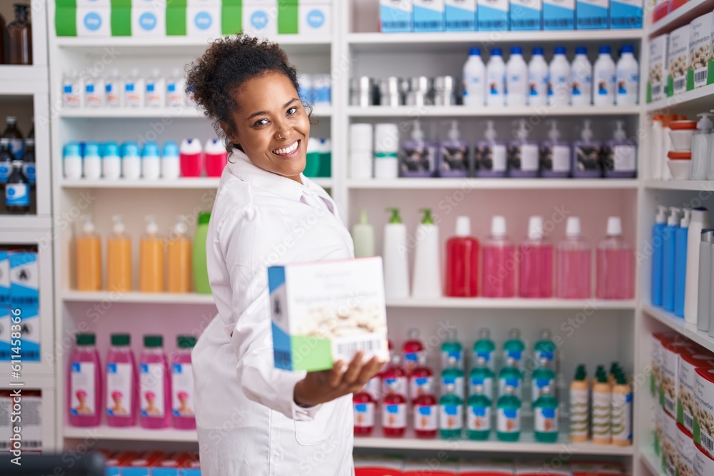 African american woman pharmacist smiling confident holding vitamin package at pharmacy