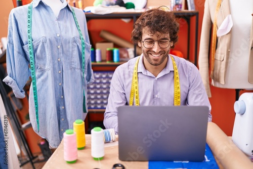 Young hispanic man tailor smiling confident using laptop at atelier