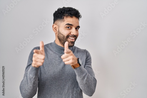 Hispanic man with beard standing over white background pointing fingers to camera with happy and funny face. good energy and vibes. © Krakenimages.com