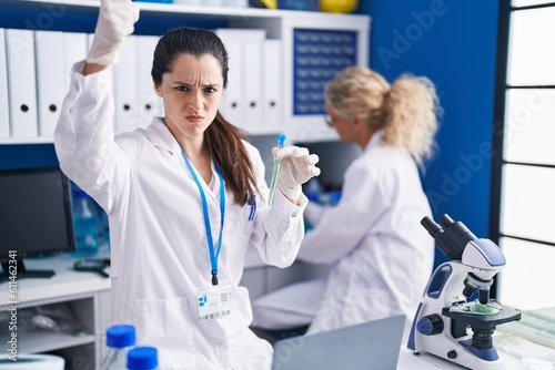 Young hispanic woman working at scientist laboratory annoyed and frustrated shouting with anger, yelling crazy with anger and hand raised