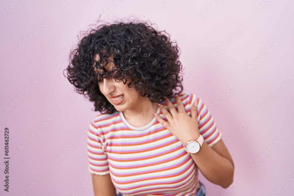Young middle east woman standing over pink background suffering of backache, touching back with hand, muscular pain Young middle east woman standing over pink background suffering of backache, touching back with hand, muscular pain
