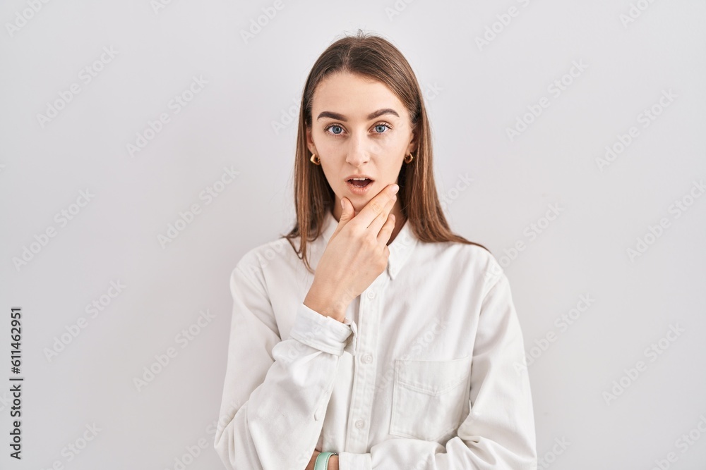 Young caucasian woman standing over isolated background looking fascinated with disbelief, surprise and amazed expression with hands on chin Young caucasian woman standing over isolated background looking fascinated with disbelief, surprise and amazed expression with hands on chin