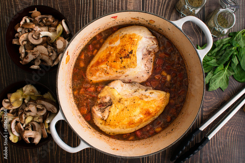Browned Chicken Breasts and Tomato Sauce in a Dutch Oven: Seared chicken breasts surrounded by basil, wild mushrooms, and other ingredients