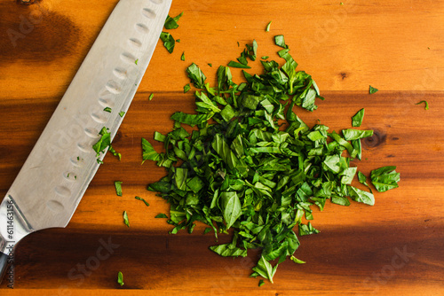 Chopped Basil with a Chef's Knife on a Wooden Cutting Board: Prepped Genovese basil leaves on a wood chopping board with a santoku knife