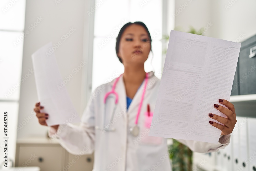 Young chinese woman wearing doctor uniform reading document at clinic Young chinese woman wearing doctor uniform reading document at clinic
