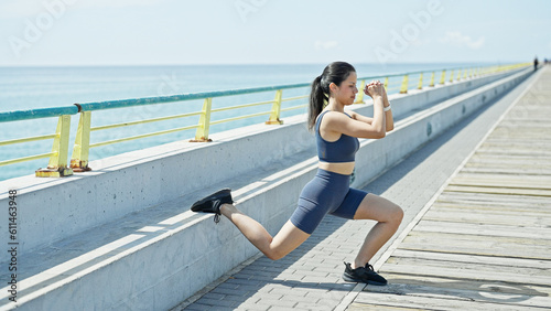 Young beautiful hispanic woman wearing sportswear training legs exercise at seaside