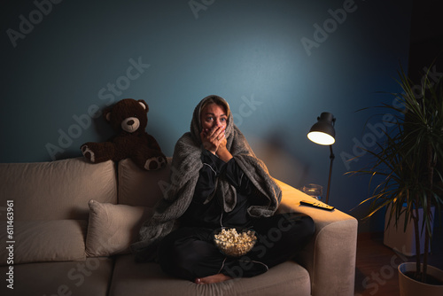 A girl home alone, spellbound by a horror film. Wide-eyed, she leans in, captivated by the flickering TV glow, engrossed in the terrifying narrative. Shadows amplify the suspense, making for an intens