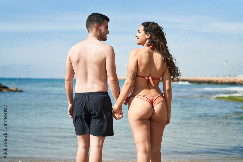 Young hispanic couple tourists wearing swimsuit standing with hands together at seaside