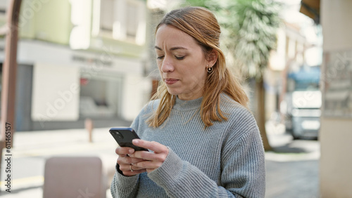 Young blonde woman using smartphone with serious expression at street