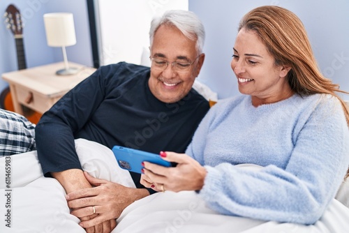 Middle age man and woman couple using smartphone lying on bed at bedroom