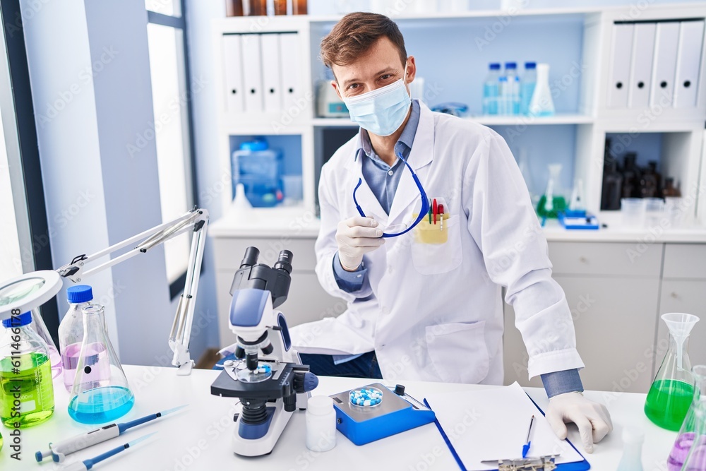 Young man scientist wearing medical mask sitting on table at laboratory Young man scientist wearing medical mask sitting on table at laboratory