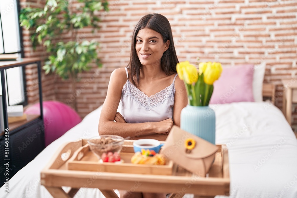 Brunette young woman eating breakfast sitting on the bed happy face smiling with crossed arms looking at the camera. positive person.