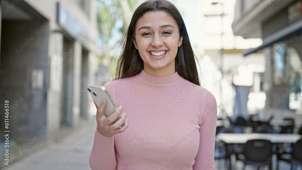 Young beautiful hispanic woman smiling confident using smartphone at street