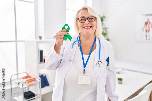 Middle age caucasian woman holding support green ribbon looking positive and happy standing and smiling with a confident smile showing teeth