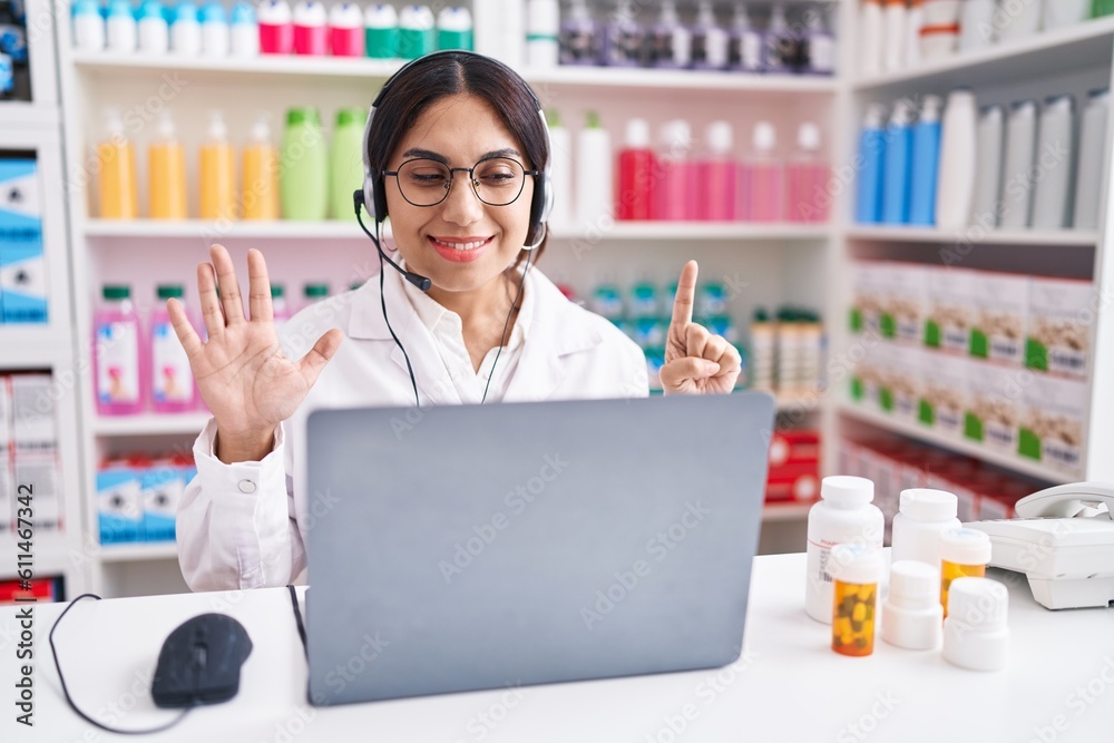 Young arab woman working at pharmacy drugstore using laptop showing and pointing up with fingers number six while smiling confident and happy.
