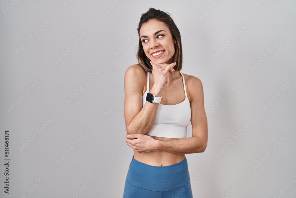 Hispanic woman wearing sportswear over isolated background with hand on chin thinking about question, pensive expression. smiling and thoughtful face. doubt concept. Hispanic woman wearing sportswear over isolated background with hand on chin thinking about question, pensive expression. smiling and thoughtful face. doubt concept.