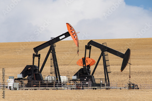 Two colorful black and orange oil field pumpjacks, or donkeys, in a dirt field against a cloudy sky