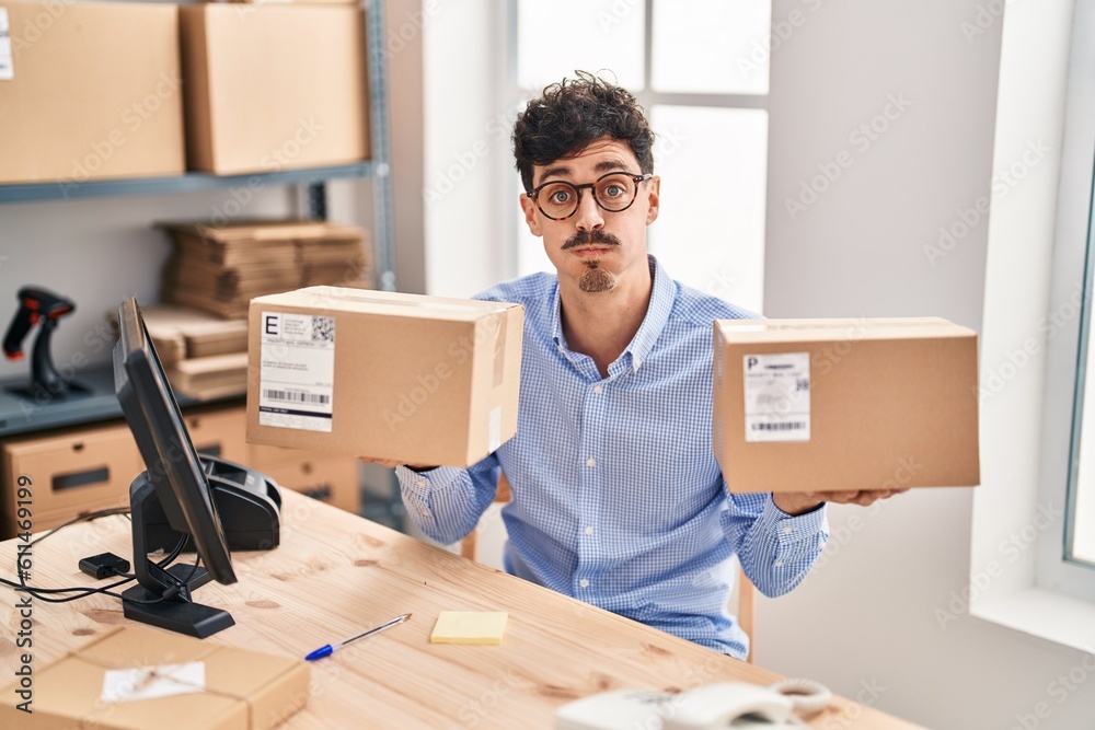 Hispanic man working at small business ecommerce holding packages puffing cheeks with funny face. mouth inflated with air, catching air. Hispanic man working at small business ecommerce holding packages puffing cheeks with funny face. mouth inflated with air, catching air.