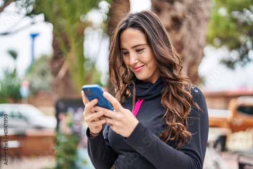 Young hispanic woman wearing sportswear using smartphone at park