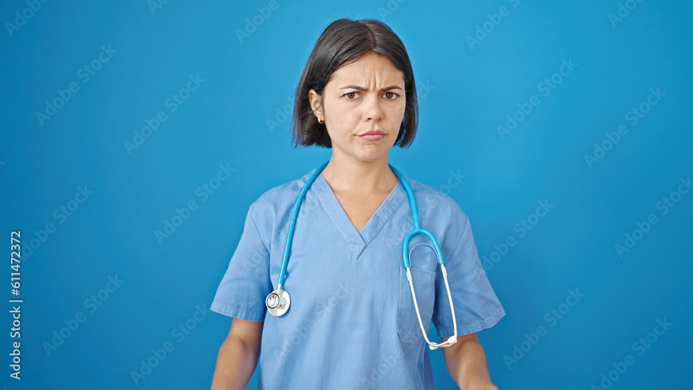 Young beautiful hispanic woman doctor standing with serious expression over isolated blue background Young beautiful hispanic woman doctor standing with serious expression over isolated blue background