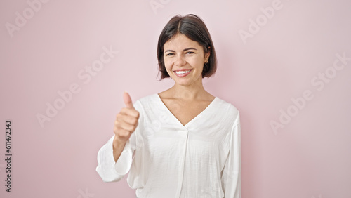 Young beautiful hispanic woman smiling with thumb up over isolated pink background