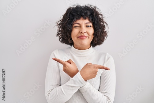 Hispanic woman with curly hair standing over isolated background pointing to both sides with fingers, different direction disagree