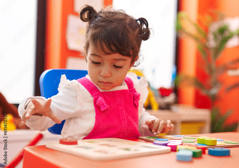 Adorable hispanic girl playing with maths puzzle game sitting on table at kindergarten Adorable hispanic girl playing with maths puzzle game sitting on table at kindergarten