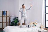 Young hispanic man standing on bed dancing at bedroom