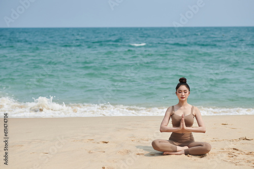 Fit woman meditating in lotus position on sandy sea beach
