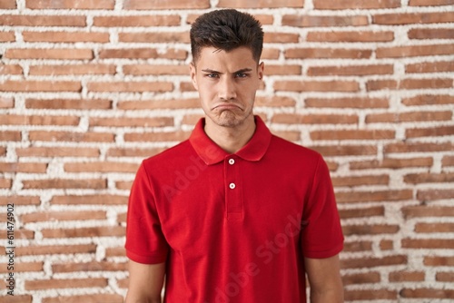Young hispanic man standing over bricks wall depressed and worry for distress, crying angry and afraid. sad expression.