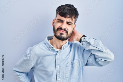Young hispanic man with beard standing over blue background suffering of neck ache injury, touching neck with hand, muscular pain © Krakenimages.com