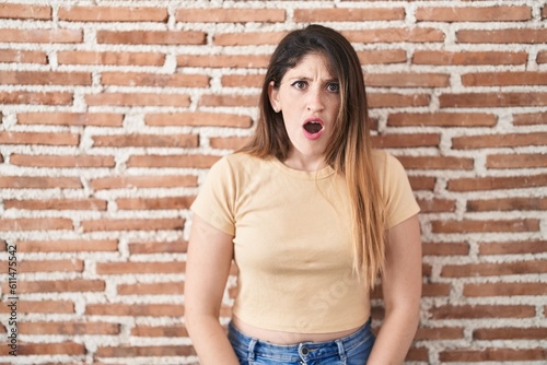 Young brunette woman standing over bricks wall in shock face, looking skeptical and sarcastic, surprised with open mouth © Krakenimages.com